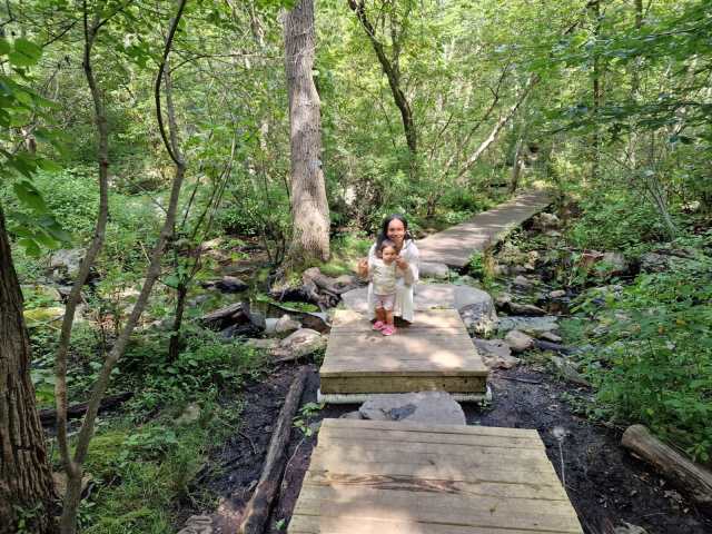 woman and little girl standing in a small bridge in the middle of the forest.