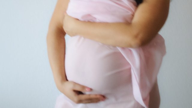 Pregnant woman holding her stomach, wearing a light pink transparent cover-up.