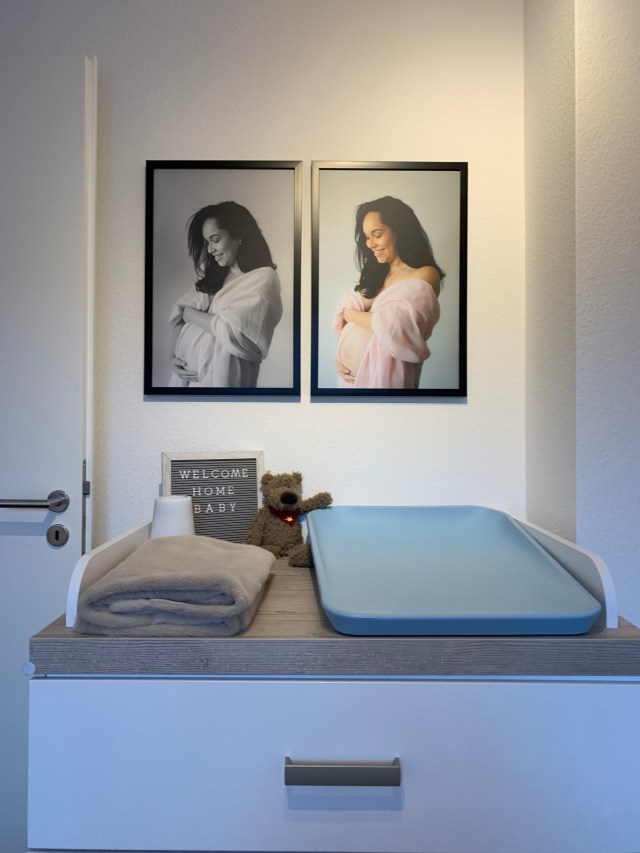 Photo of a baby changing table which includes baby accessories at the top of changing table and two photos on the wall above the changing table.