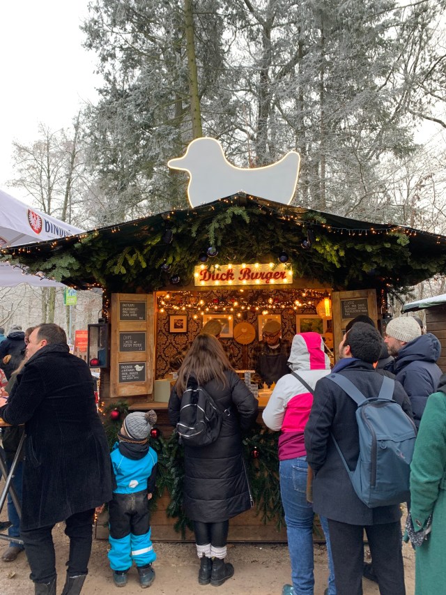 A small crowd of people patiently waiting in life in front of a Christmas market stand in Frankfurt, Germany.