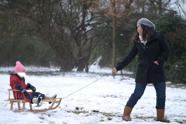 A happy mother pulling her daughter on a sleigh ride.