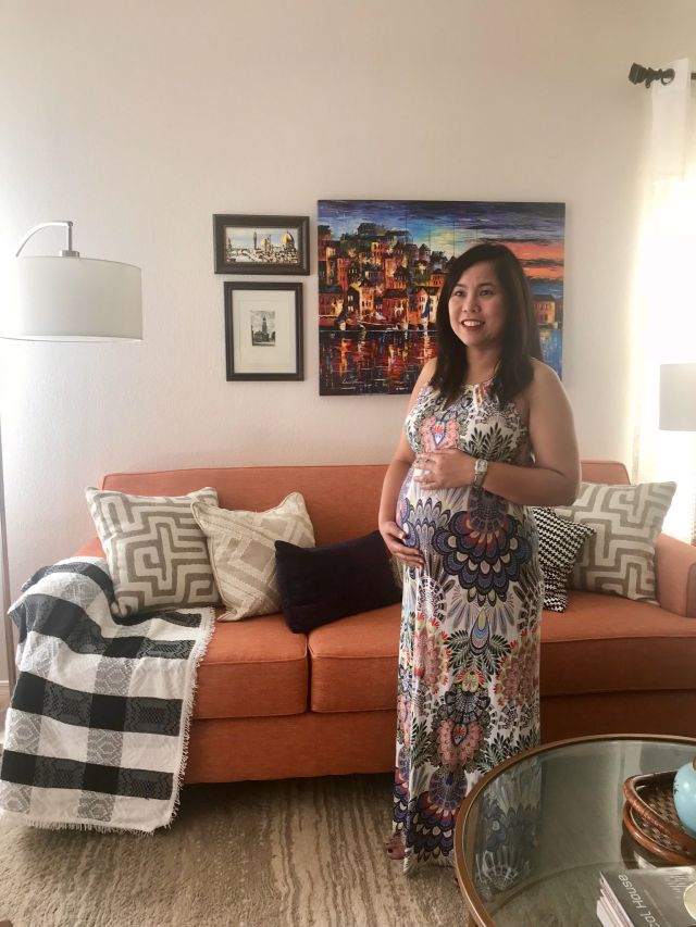 Pregnant woman standing smiling while holding her belly showing how far she is along her pregnancy.